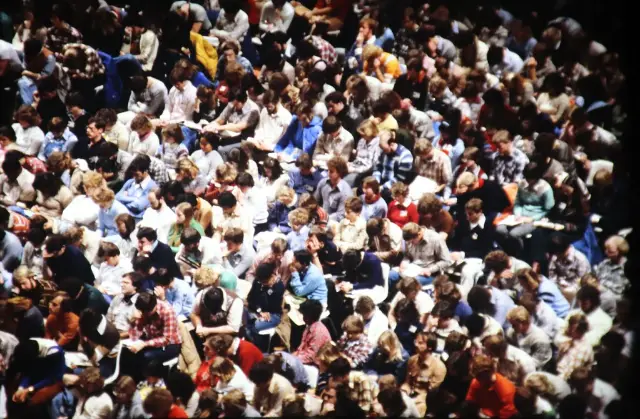 A packed assembly hall, the audience reading handouts